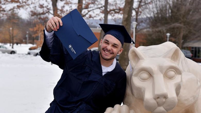 A recent graduate poses with at the Nittany Lion Shrine following commencement