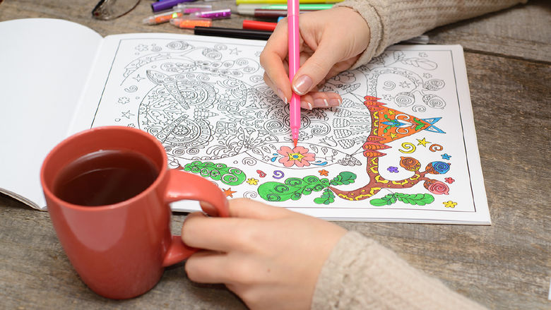 A person coloring while drinking coffee