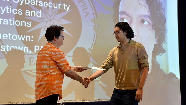 Hans Esteban, cybersecurity analytics and operations major, accepts his certificate and pin at the induction ceremony. 