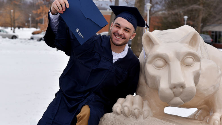 A recent graduate poses with at the Nittany Lion Shrine following commencement