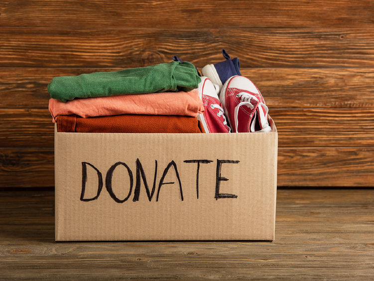 A cardboard box marked with the word donate filled with clothes and shoes