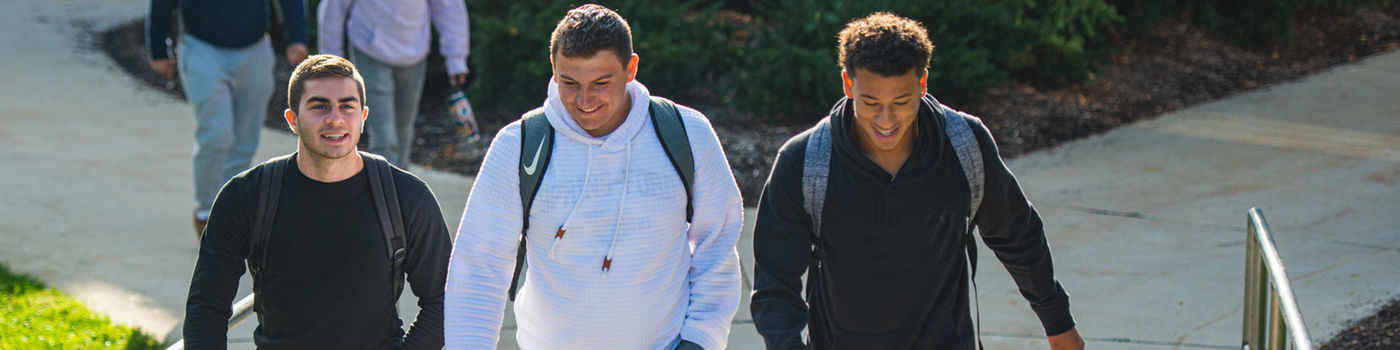 Three male students walking on campus near the Hawthorn Building