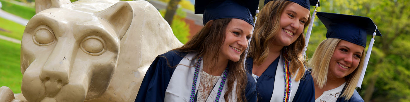 Three female graduates pose at the lion shrine on the Penn State Altoona campus.