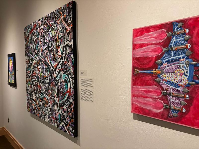 Art gallery wall with three colorful abstract paintings, including bold red, graffiti-style, and vibrant fantasy-themed works.