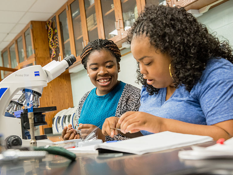 Two female students seated before a microscope in a biology class