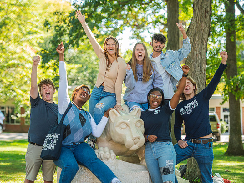 Students cheering while sitting on the Lion Shrine statue