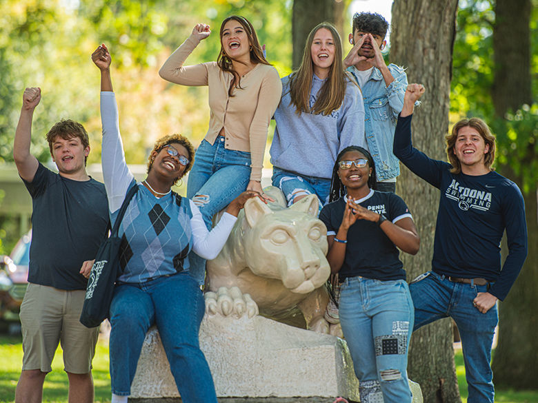 A group of diverse students cheering around the Nittany Lion Shrine