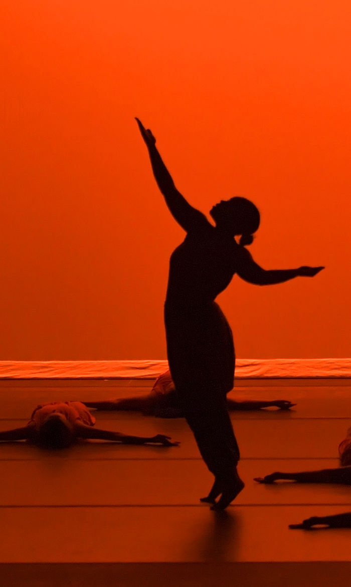 A dancer in silhouette in front of an orange background