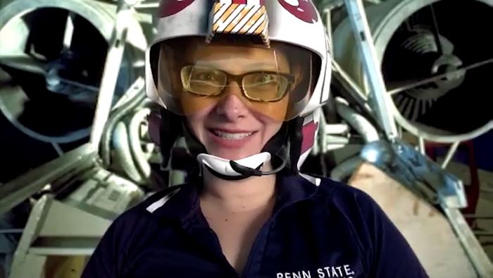 Penn State Behrend professor Charlotte de Vries wears a prop helmet while teaching in front of a spaceship-themed backdrop.