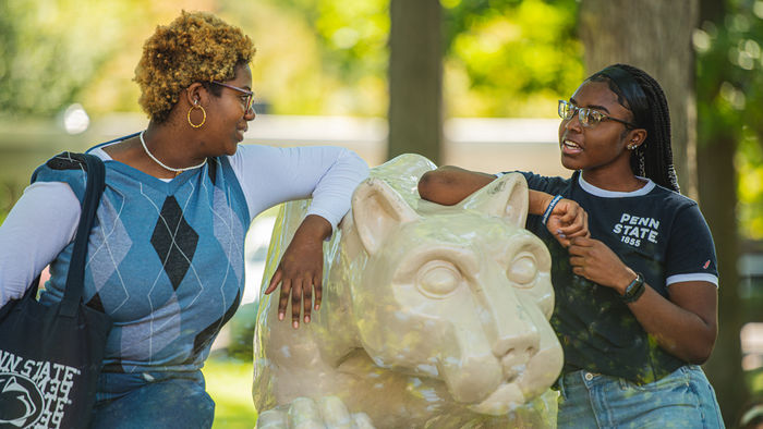 Two female students have a conversation while hanging out at the lion shrine