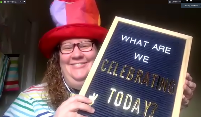 A woman smiles with a rainbow-striped hat and holds up a letter board saying, "what are we celebrating today?"