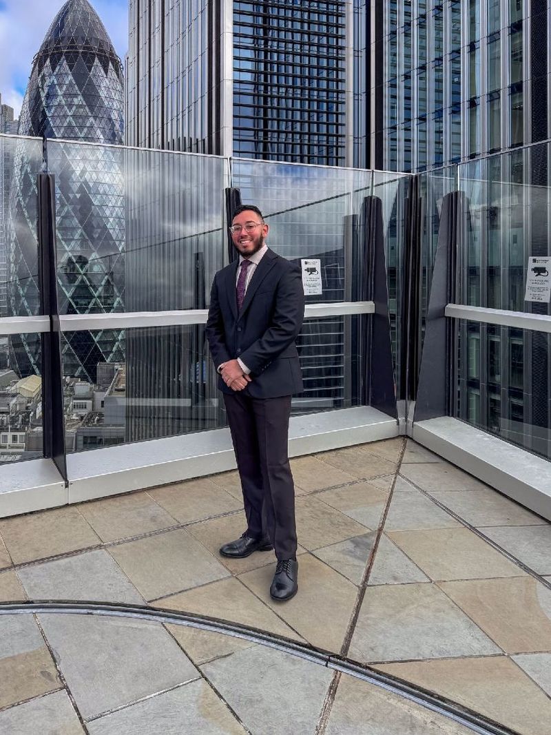 A student wearing a suit stands on a rooftop in London
