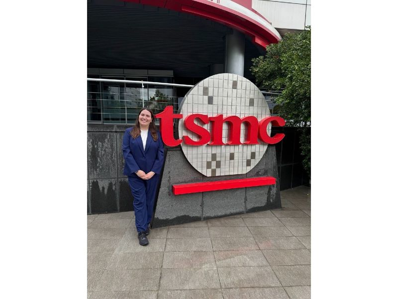 A student stands in front of a company sign that reads "tsmc"