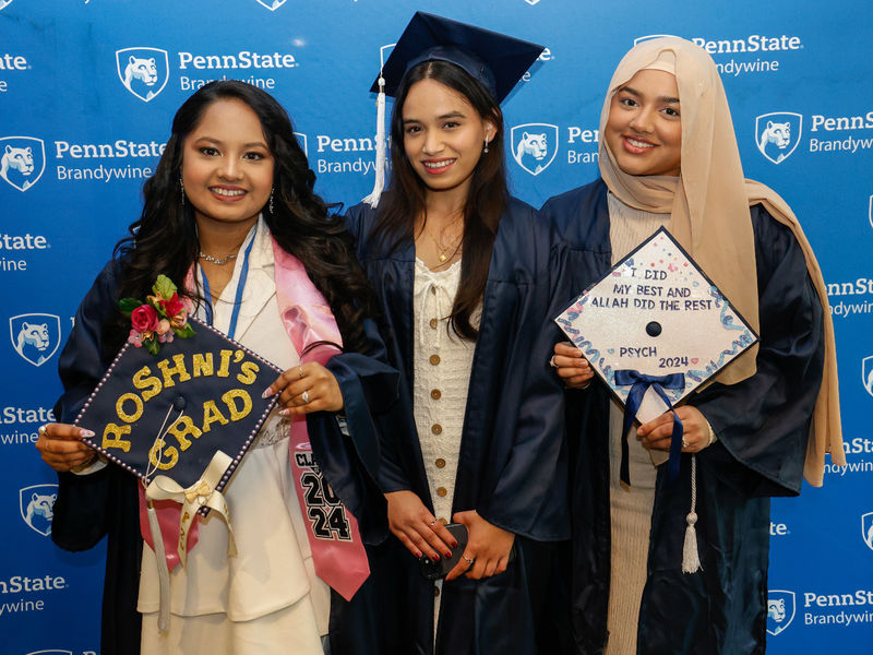 Three female students pose for a photo wearing their commencement gowns.
