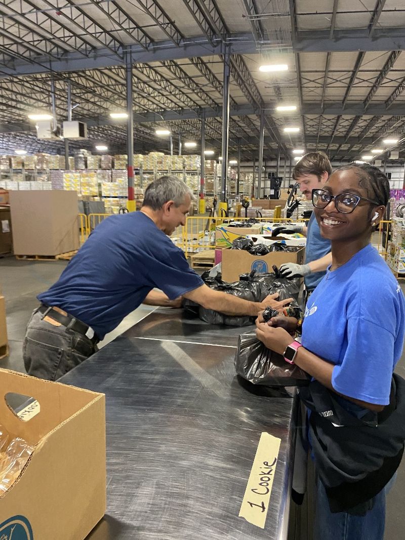 A student wearing a blue shirt ties a prepared food bag for local schoolchildren during an alternative spring break trip