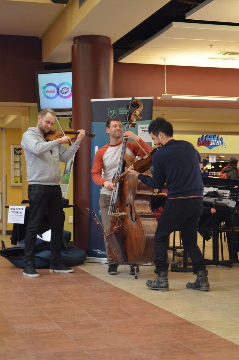 Three string musicians smile while they perform in a cafeteria.