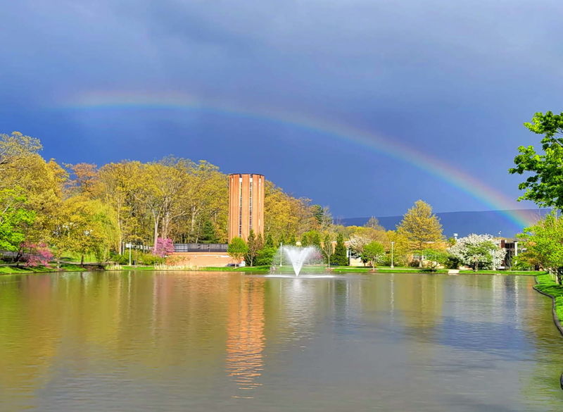 A rainbow against a dark sky over a pond on a college campus