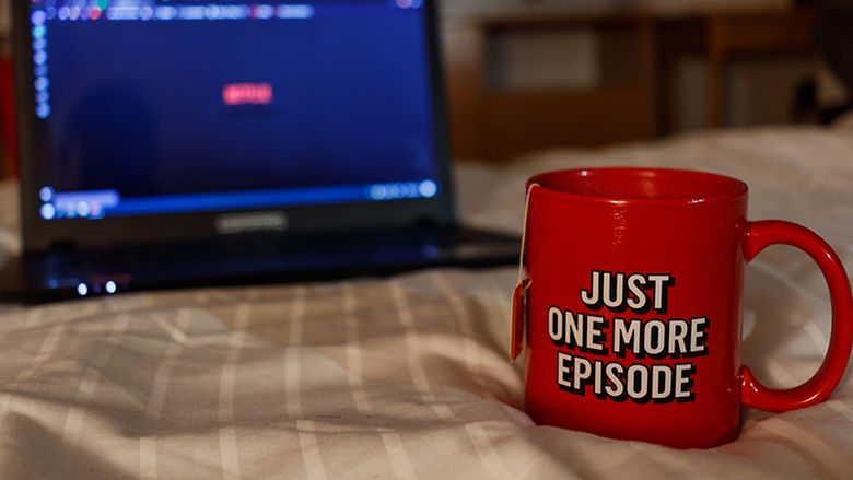 A tea mug reading Just one more episode sitting just in front of a laptop