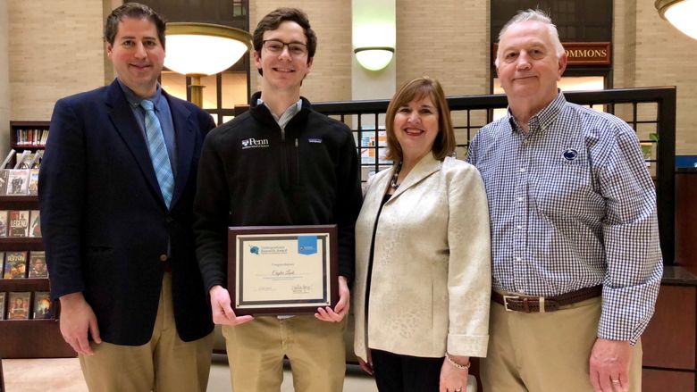 group of four people standing with male student in center holding award plaque