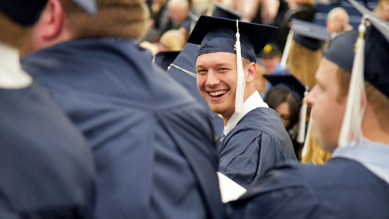 A graduate at Penn State Altoona's spring 2022 commencement ceremony spots the campus photographer and smiles for a photo