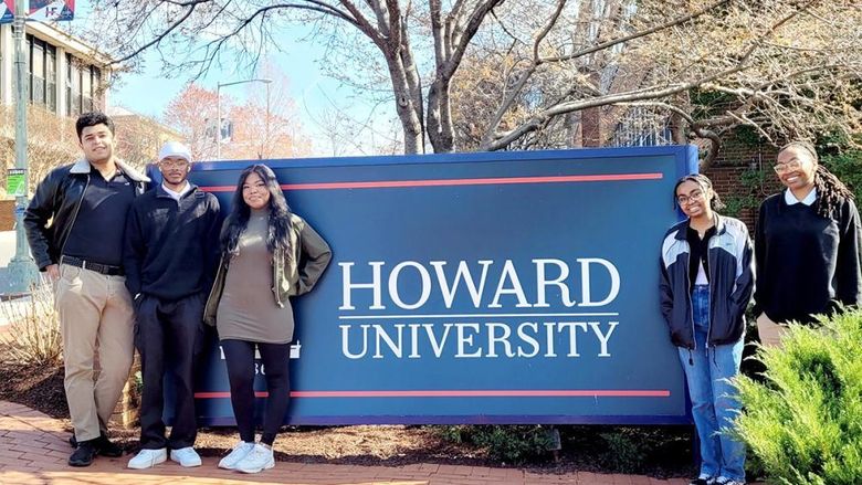 Five students pose in front of a Howard University sign