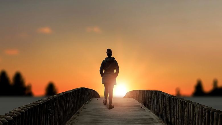 a woman stands on bridge over a lake at sunset
