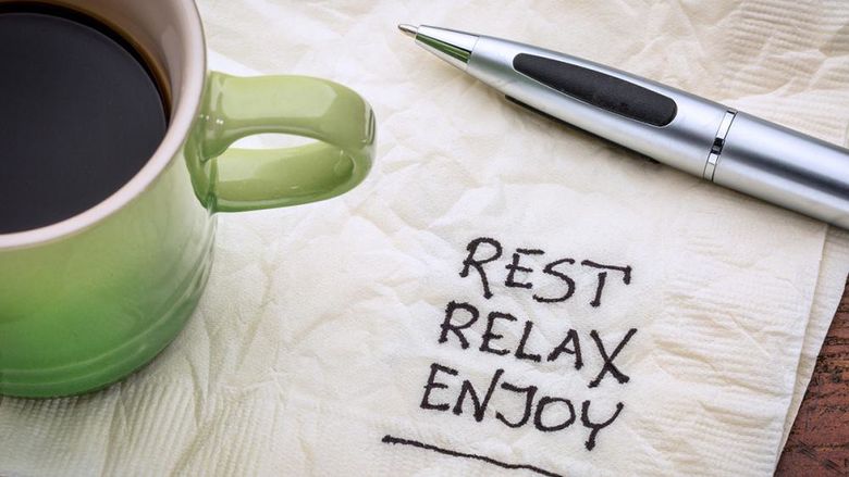 Rest, relax, and enjoy written on a napkin with a cup of coffee in the corner