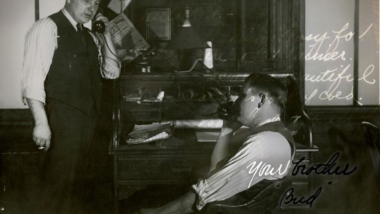 A black-and-white photo from September 9, 1942, shows two men in an office, each on the phone. The man on the left stands with a cigarette, while the man on the right is seated. The background features a cluttered desk. The image includes handwritten text and is signed Your brother, Bud.
