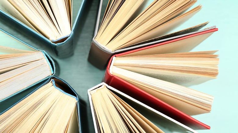 Six books are arranged in a circle, all open with pages fanned out, showing their spines and covers in various colors against a light turquoise background.