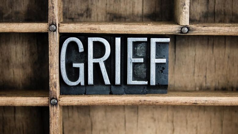 The image shows the word GRIEF spelled out in metal letterpress blocks placed within a wooden compartment, evoking a strong, somber emotion.