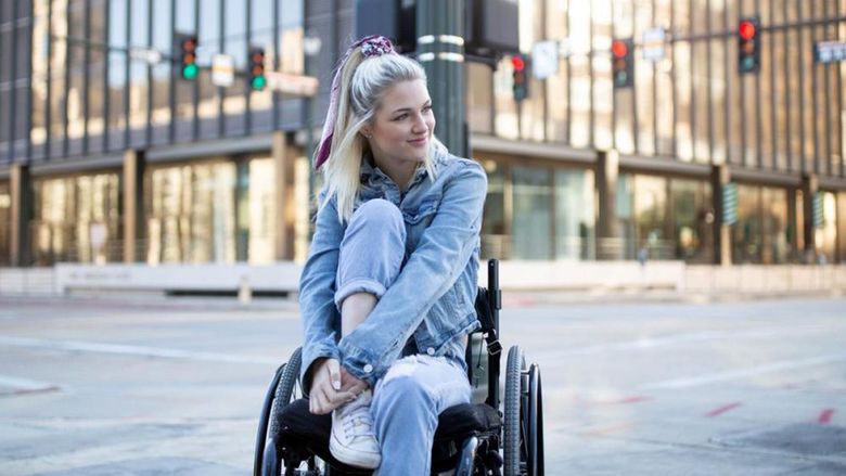 A young woman in a wheelchair with a large city building in the background