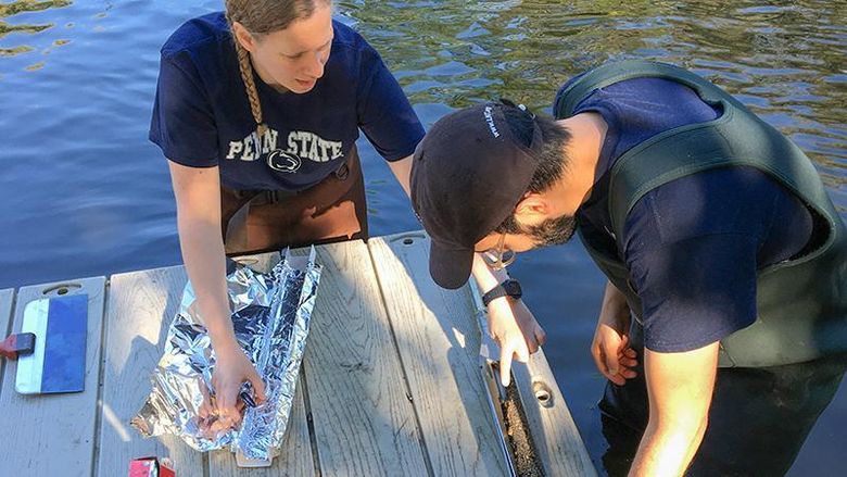 Two people standing in the water by a dock examining a dirt core from the ground
