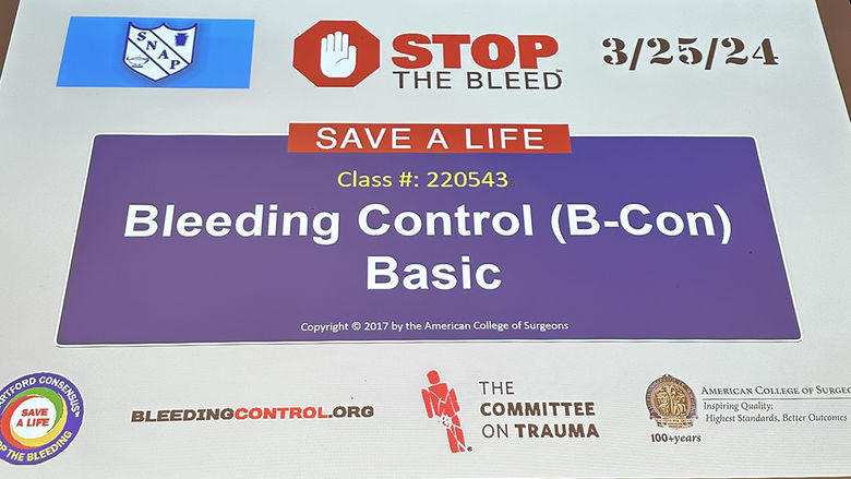 A presentation slide displays information about a Stop the Bleed training session, specifically the Bleeding Control (B-Con) Basic course. The slide includes the date 3/25/24 and the class number 220543. It features logos from the Student Nurses Association of Pennsylvania (SNAP), the American College of Surgeons, and The Committee on Trauma, along with the website BleedingControl.org. The slide emphasizes the importance of saving lives through bleeding control education.