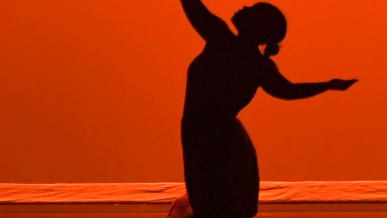 A dancer in silhouette in front of an orange background