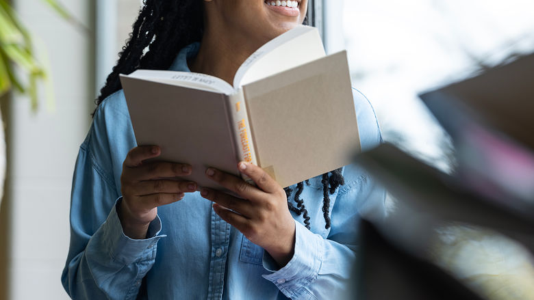 A student looks out a window over the reflecting pond while reading a book in the Penn State Altoona Eiche Library