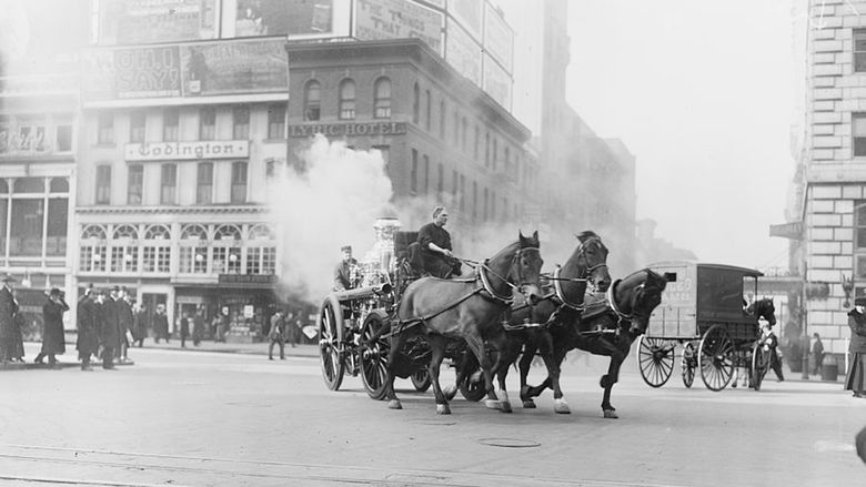 A horse-drawn fire vehicle turns the corner at the intersection of West 43rd Street and Broadway in New York City about a century ago.