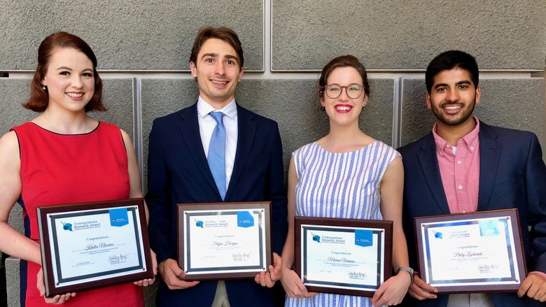 four students standing and holding award plaques