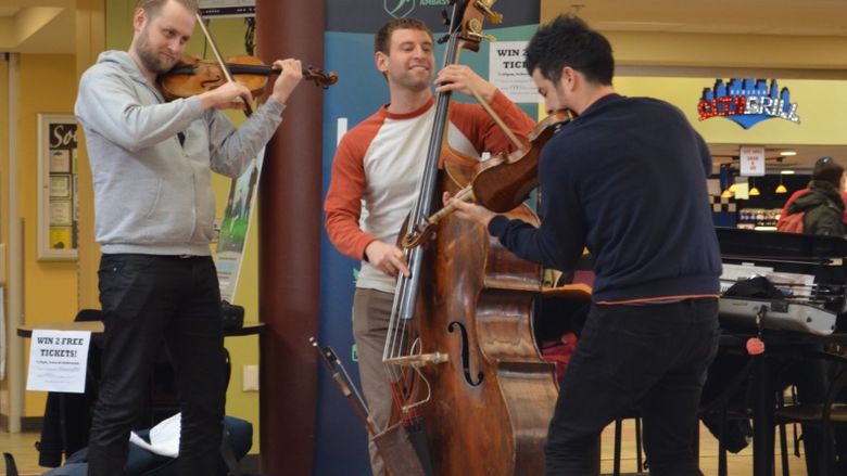 Three string musicians smile while they perform in a cafeteria.
