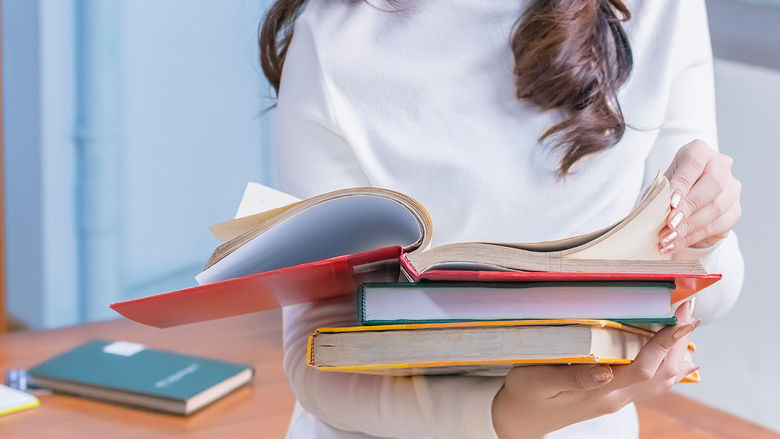 A student reads a book stacked on top of other books.