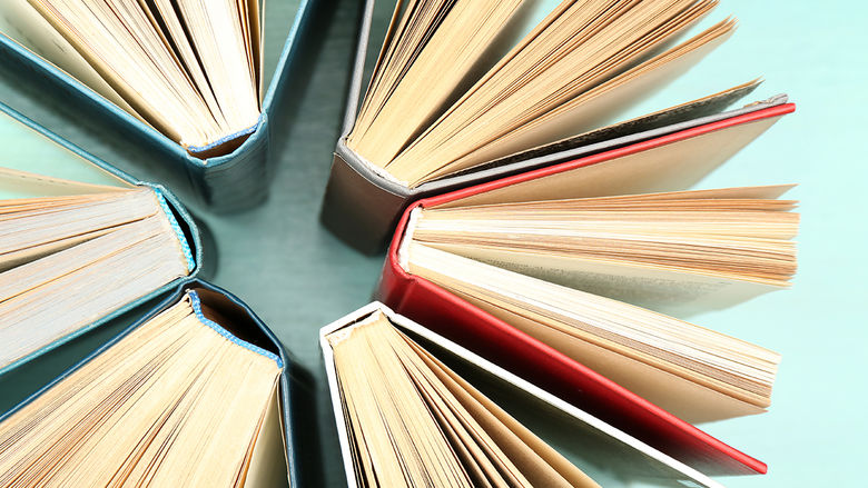 Six books are arranged in a circle, all open with pages fanned out, showing their spines and covers in various colors against a light turquoise background.