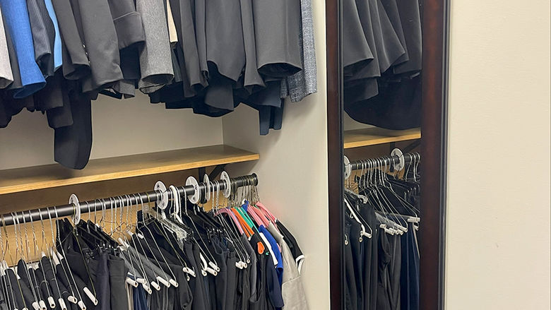 A full-length mirror hanging on a wall near a double-decker rack of men's suit jackets