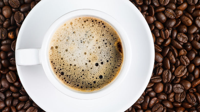 A cup of coffee sitting among coffee beans