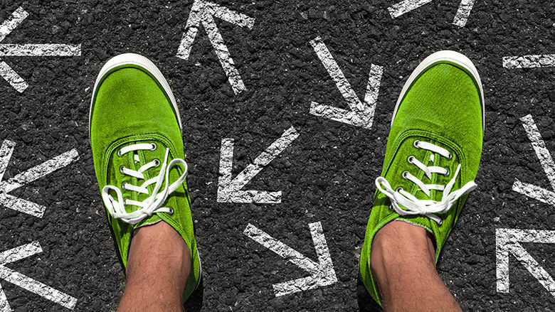 A pair of feet standing on pavement with arrows drawn in chalk pointing in multiple directions