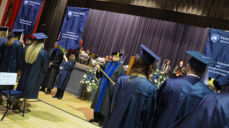 College Marshal Bill Engelbret (center) looks on as graduates, faculty, and staff process.