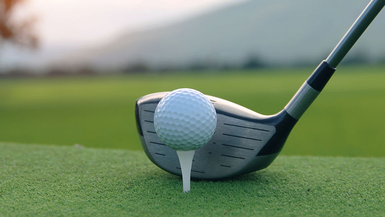 A golf ball on a tee with a golf club ready to hit it