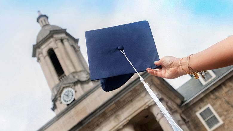 A hand holding a graduation cap in front of Old Main