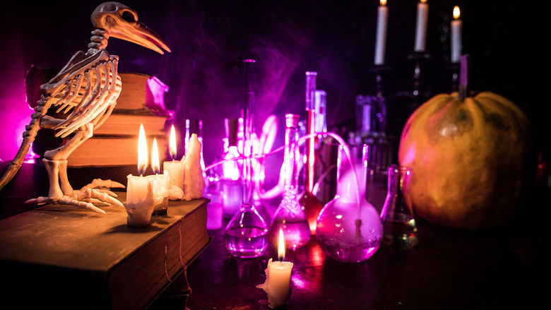 A spooky scene with a bird skeleton, glowing lab beakers, candles, and a pumpkin, set against a dark, eerie background with vibrant purple lighting.