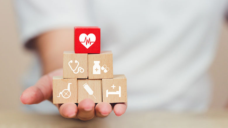A hand holding building blocks representing different aspects of healthcare
