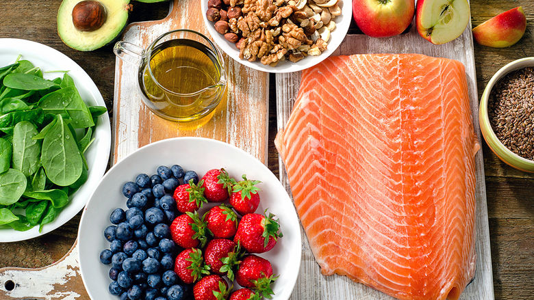 a wooden table laden with many health foods, including salmon, berries, greens, and oats