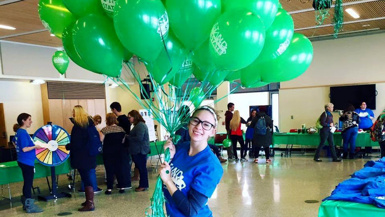 Gabrielle Davidson poses with a cluster of balloons at a Stand for State bystander intervention event.